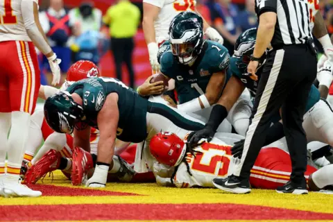 Getty Images The Philadelphia Eagles pile over the line in their dark green outfits while a number of Kansas City Chiefs players lie sprawled on the ground