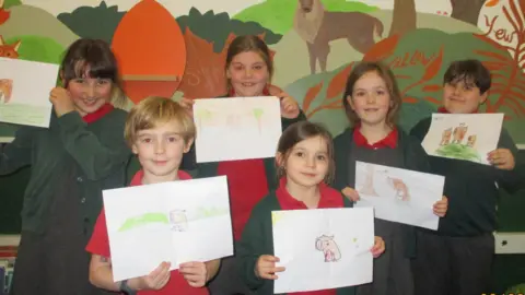 Twyford Primary School A group of schoolchildren in uniform hold up pictures of capybaras. 
