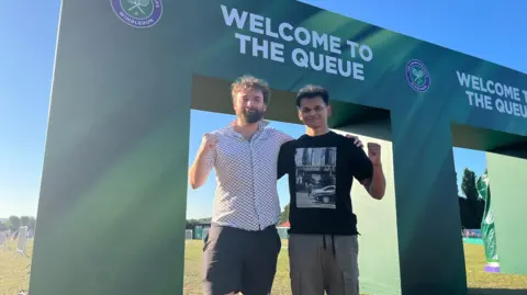 PA Friends Francis and Dhillon standing by the 'welcome to the queue sign'