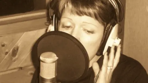 Lianne Morgan A woman in a studio singing in front of a professional microphone. She has short hair and the picture is in black and white. 