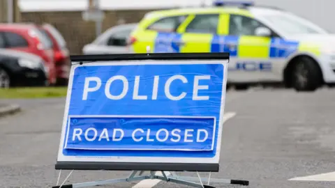 Getty Images Police vehicle parked behind a blue police accident sign 