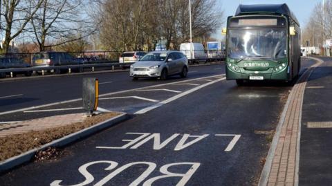 A green bus using a lane with 'Bus Lane' painted on the carriageway