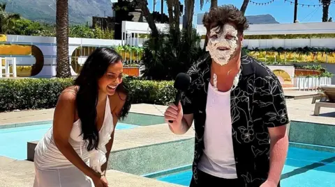 Morgan James Morgan James with cream on his face while Maya Jama is next to him laughing.