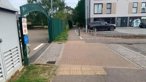 A cycle path in Mead Drive, Kesgrave, where a man was stabbed. The cycle path is in the foreground, with the left turn to Kesgrave Community Centre nearby. A small car park and flats are further along