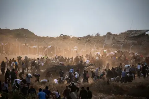 Getty Images People carry relief supplies from the Gaza Humanitarian Foundation (GHF) - the picture shows lots of people, some with sacks on their backs