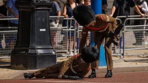 Getty Images A foot guard is lifted up by another member of the Army after he fainted on the Mall