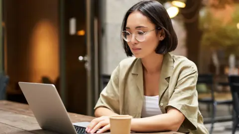 A young woman working on her laptop and drinking coffee at a cafe