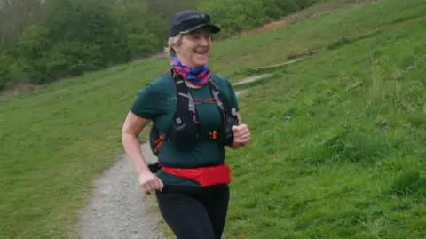 Amanda Cooper/parkrun Amanda Cooper out on a run with grassy banks either side.