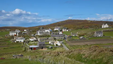 MANX SCENES Cregneash village, which has a mix of thatched cottages and slate roofed buildings set in the countryside with a hill behind.