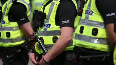 Police Scotland officers wearing hi-viz vests over black polo shirts displaying the name of the force in white writing on the sleeve.