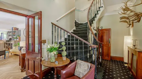 Fine & Country Scotland A hallway in a luxury hotel with a winding staircase, dark carpet and lots of wooden doors and panelling