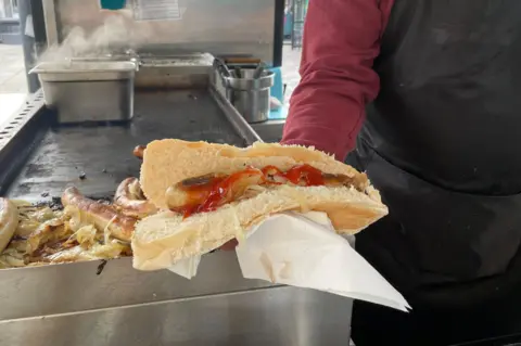 Caroline Lowbridge/BBC Charlie holds up a hotdog