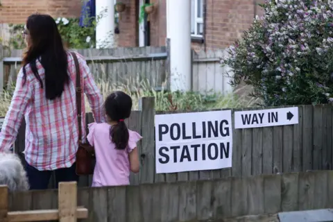 Getty Images A woman and a young child wearing pink walk into a polling station