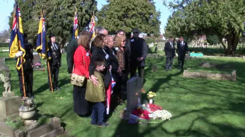 The family and military personnel gathered around the gravestone at the cemetery. 