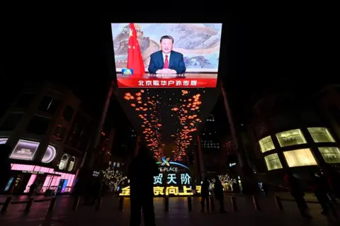 ADEK BERRY/AFP Uma grande tela mostra o presidente chinês, Xi Jinping, fazendo um discurso antes das celebrações da véspera de Ano Novo em Pequim, em 31 de dezembro.