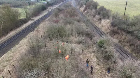 Network Rail A number of volunteers working between two railway tracks, the photo is taken from above, and shows about nine people, working from a distance. 