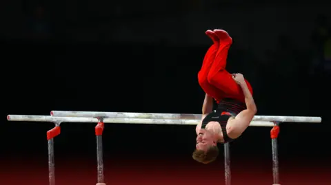PA Harry Eyres, wearing red trousers, is mid back-flip during a gymnastics routine