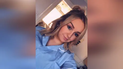 Jess Thorpe Jessica Thorpe in her nurse uniform, slightly smiling at the camera while taking a selfie.