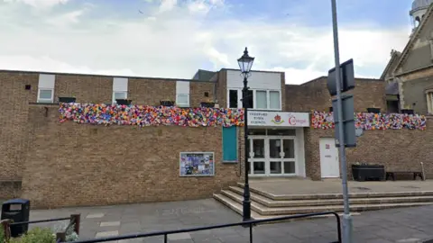 Thetford Town Council building which is made of brown bricks. The entrance of the building is to the right of the image, and has white doors which say Thetford Town Council above. 