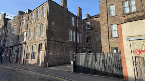 A small car park on a cobbled street surrounded by buildings
