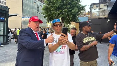 Kayla Epstein / BBC A Trump impersonator outside Madison Square Garden poses for photos with tourists and Knicks fans.