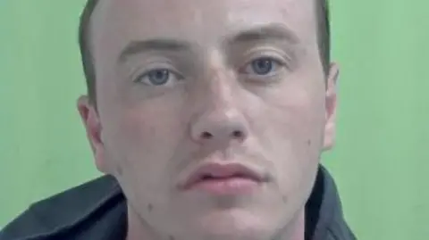 IOM CONSTABULARY Police photo of Kyle Wright, who has close-cropped brown hair and blue eyes. he is wearing a dark coloured hoodie. The background is green.