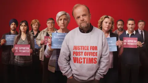ITV A promotional image for a TV drama showing a group of people in a line holding up signs saying "Support our Sub Postmasters". At the centre, a man wears a grey sweatshirt with Justice for our Post Office victims" on the front