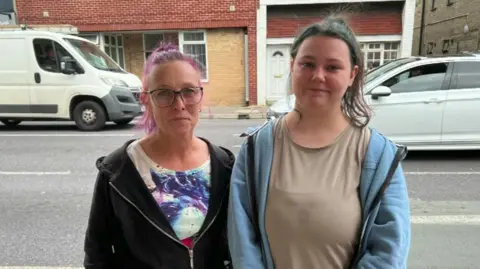 Kelly and Lou standing on a street with traffic passing in the background