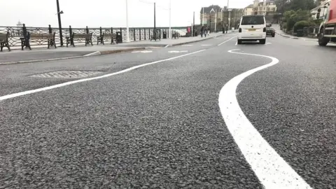 The old layout of the Clevedon seafront. There is a white wiggly line on the road. Cars can be seen on the road in the distance.