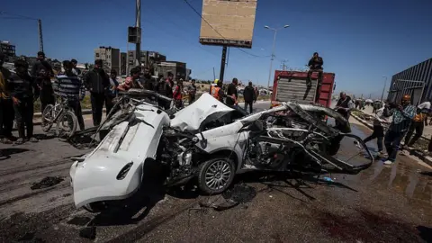 Anadolu via Getty Images Palestinian first responders and residents look at a car reportedly destroyed in an Israeli artillery strike that killed three people, in the Maghazi area of central Gaza (23 April 2026)