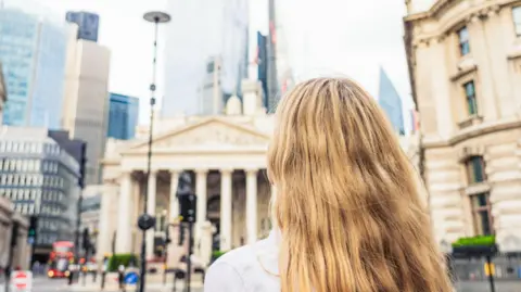 Getty Images Rear view of a young woman looking up towards the towers in the heart of the City of London, the UK's key financial district, with the Bank of England at left.