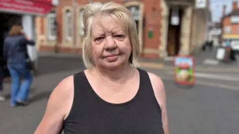 A woman with a black top and blonde hair standing in a street