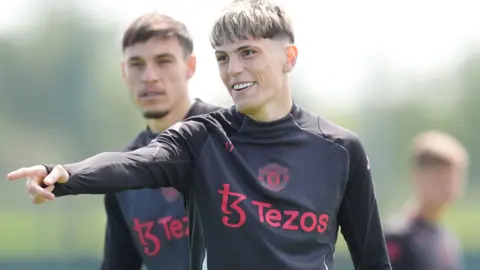 PA Media Garnacho has short dyed blonde hair and is wearing a black training top with red sponsor logo and Manchester United badge - it is a shot from training in 2025.