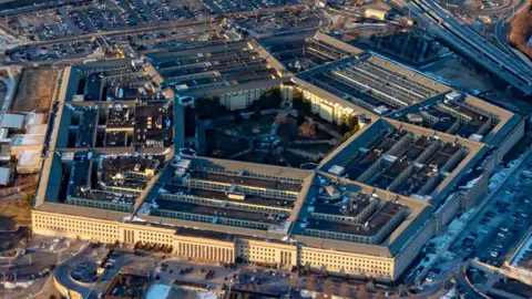 An aerial image of the Pentagon building, showing an overhead view of the building and surrounding highways and trees.
