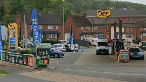 Google Maps A Google Maps street view image of the entrance to a Jet petrol station. There are cars parked in bays to the left of the image and cars parked next to the petrol pumps. Three Greggs banners can also be seen to the left of the image.