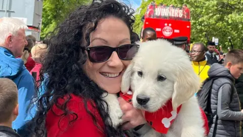 Woman, smiling, with a puppy wearing a red scarf.