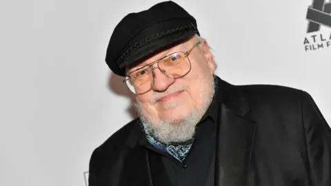 Getty Images Author George RR Martin wearing glasses and a black flat cap