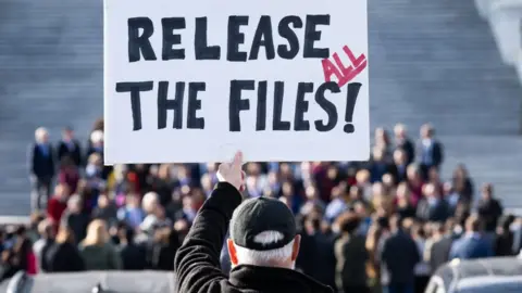 A man holds a sign reading 'Release the files' 