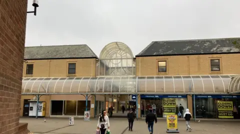 Vikki Irwin/BBC A shopping centre, which is a glass and brick building. There are shoppers in the foreground.