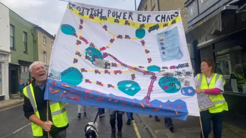 Mousumi Bakshi/BBC Campaigners wearing green high-visibility jackets holding a poster