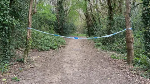 Police tape hung between two trees in woodland