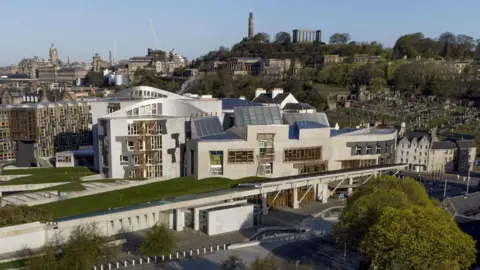 PA Media Scottish Parliament building with backdrop of Edinburgh behind 