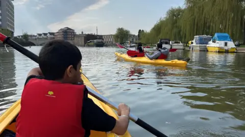 Peterborough Boat Hire Boy in a boat and other boats moored on river in Peterborough