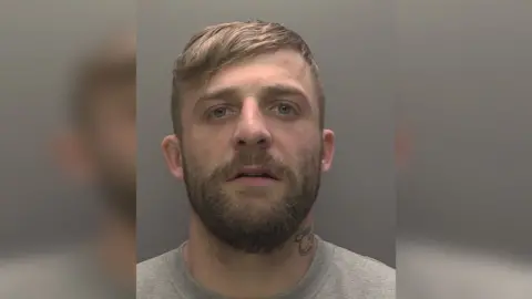 Humberside Police Police custody photograph of Ethan Armstrong who has brown hair and beard and grey shirt 