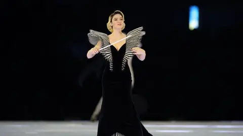 AFP via Getty Images Matilda de Angelis stands in a black gown and waving a baton