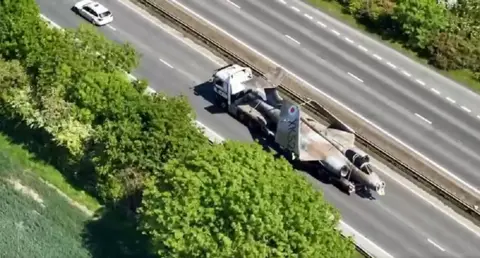 A Buccaneer fighter jet on the back of a lorry makes its way along a dual carriageway