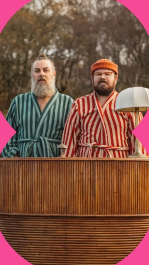 Ro and Banjo in stripy dressing gowns, standing in a wooden tub outside, with trees behind.