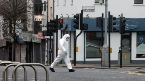 Pacemaker A forensic officer dressed in white with blue gloves on walks across a road with their head down. In the distance is a street sign for North Street in Lurgan town centre.