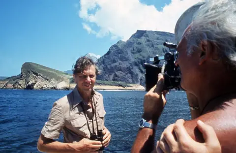 Sir David Attenborough being filmed in front of the sea and mountains for Life on Earth in 1979
