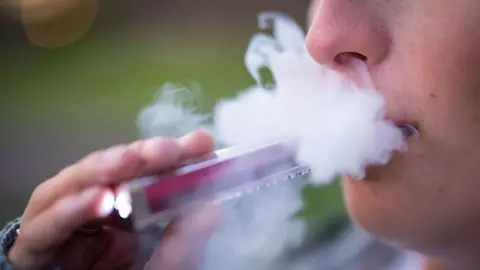 A person holds a vape up to their mouth